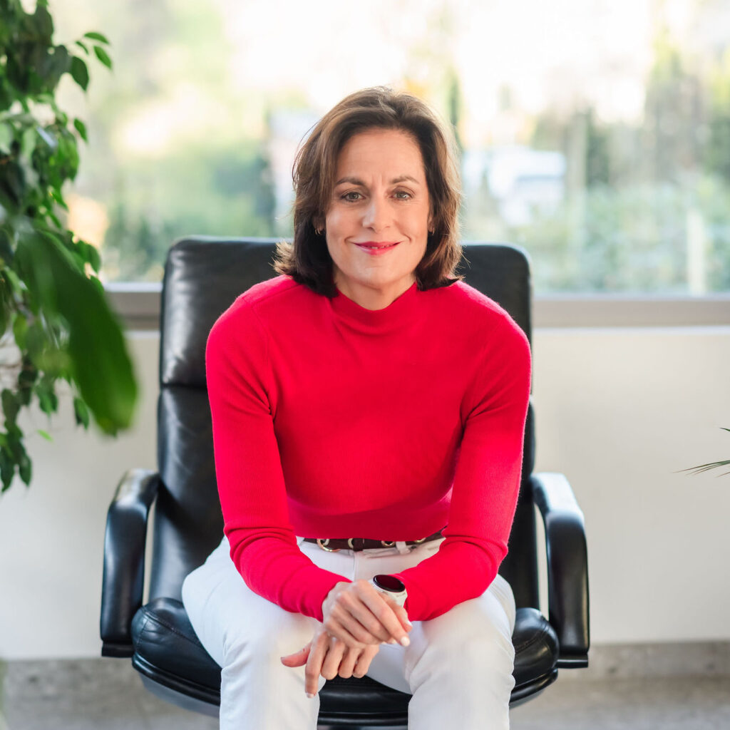 Deb sitting in an office chair, leaning forward with a warm and professional smile, reflecting the clarity and direct guidance of her method.